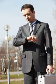 Portrait of elegant businessman looking at his watch outdoors
