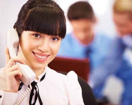 Pretty secretary speaking on the phone and looking at camera