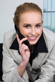Smiling blond business lady in fashion gray suit is talking by her cell phone