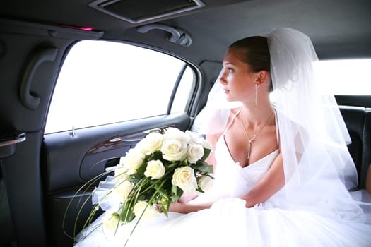 Portrait of beautiful bride with rose bouquet in hands sitting in the car and looking aside