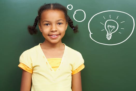 Portrait of smart girl by the blackboard thinking of light idea and looking at camera