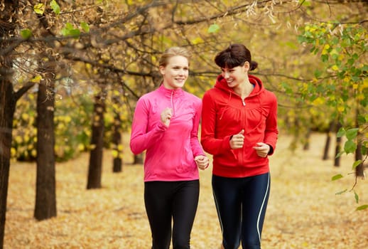 Two girls jogging in autumn park and smiling