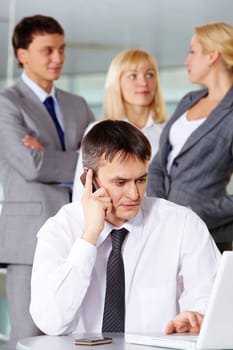 Portrait of businessman phoning and working with laptop on background of his partners