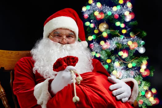 Santa sitting with a sack at the Christmas tree