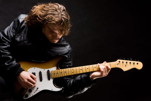 Portrait of young modern guitarist playing instrument on black background