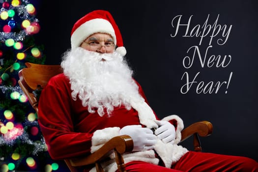 A card with Santa sitting in the armchair at the Christmas tree and the text Happy New Year