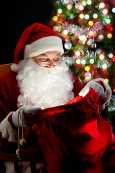 Santa sitting at the Christmas tree and looking into the sack