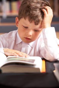 Image of cute schoolkid reading book in the library