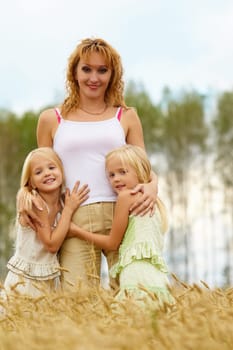 Portrait of cute twins embracing their mother with smiles in wheat field