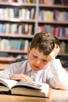 Vertical image of interested schoolkid reading book in the library