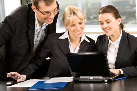 Group of three business people looking at monitor of a laptop