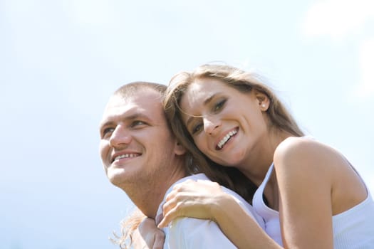 Laughing female embracing her husband on background of blue sky