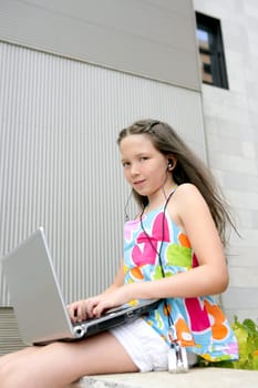 Beautiful brunette teen little girl laptop city gray background