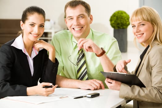 Photo of friendly business people sitting at table and looking at camera during working meeting