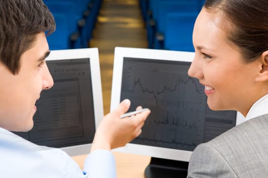 Successful businessman explaining something to his pretty colleague while they looking at each other in front of monitor