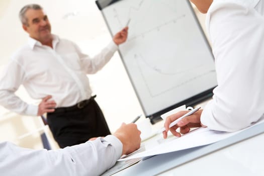 Photo of human hands over workplace on background of senior boss explaining his idea by the board