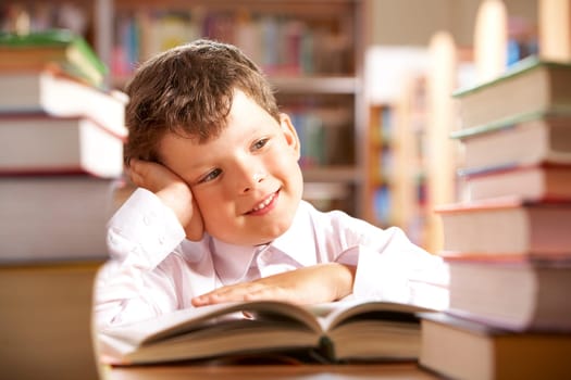 Portrait of smiling schoolboy sitting at the table with books on it