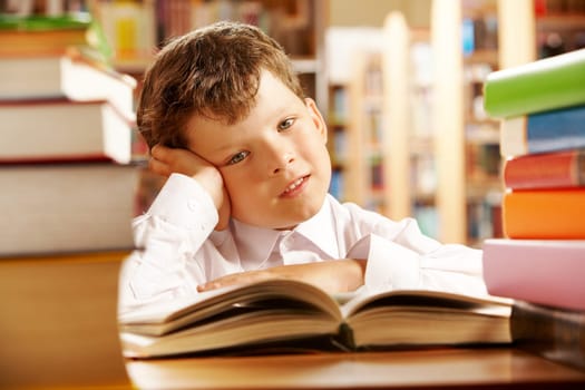 Portrait of a schoolboy sitting at table piled with books