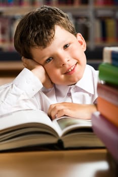 Portrait of smiling schoolboy sitting at the table with books on it