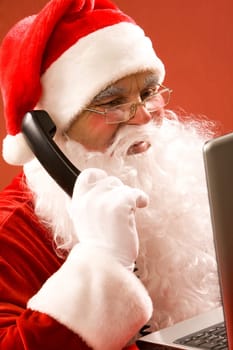 Photo of Santa Claus calling by phone with laptop in front