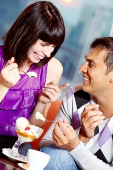 Happy girl laughing at handsome man with ice-cream drop on nose in cafe