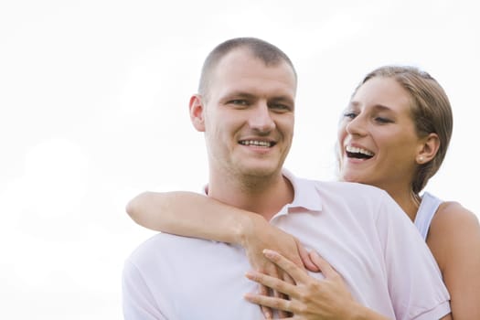 Laughing female embracing her husband on background of blue sky