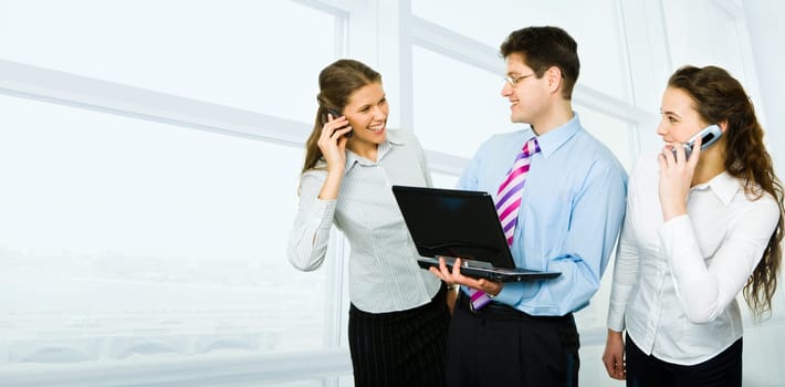 Photo of businessman standing between two women speaking on their cells and looking at each other with happy smiles