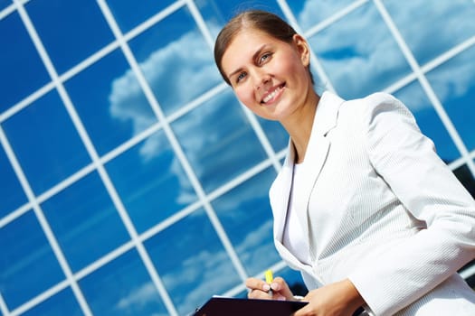 Image of pretty businesswoman with clipboard on background of modern building outdoors