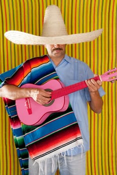 Mexican man with poncho and sombrero playing guitar typical of Mexico