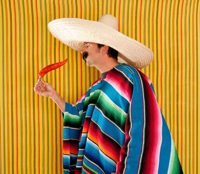 Mexican typical man eating chili hot pepper with poncho on yellow background