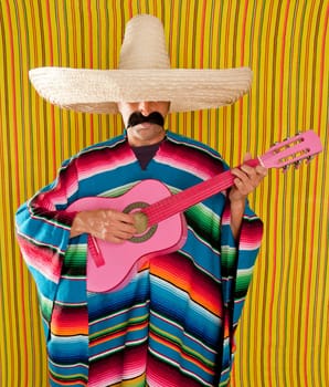 Mexican typical man with poncho and sombrero playing guitar