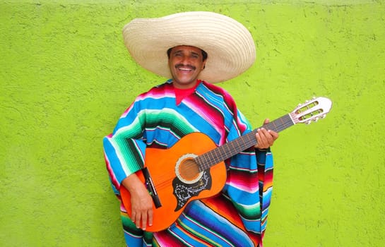 Mexican typical man playing guitar with poncho on green wall