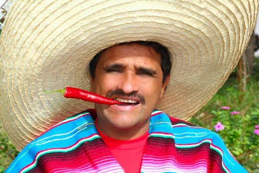 Mexican man with poncho and sombrero eating typical red chili hot pepper in Mexico