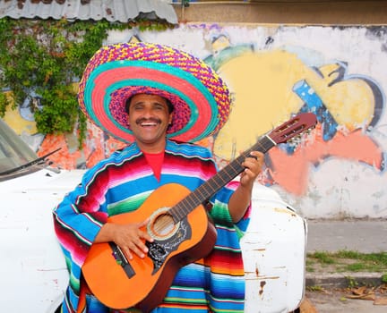 Mexican humor man smiling playing guitar sombrero poncho in street