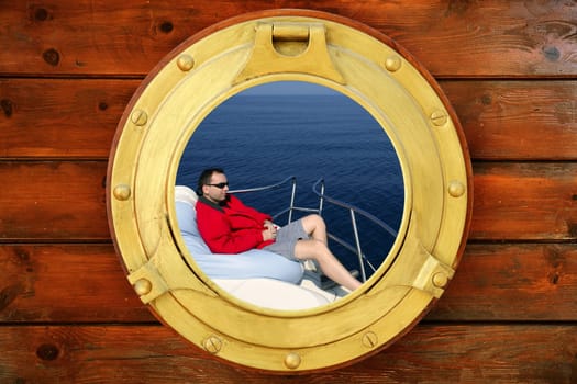 Man relaxed on bean bag over blue sea, view from boat round window
