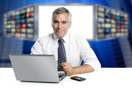gray hair tv news screen presenter laptop smiling white desk