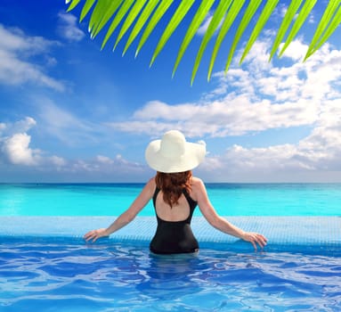 black swimsuit woman rear view in a pool with direct view to tropical Caribbean sea