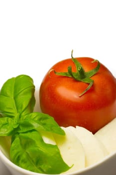 Tomato, fresh basil leaves and mozzarella in a white bowl.
