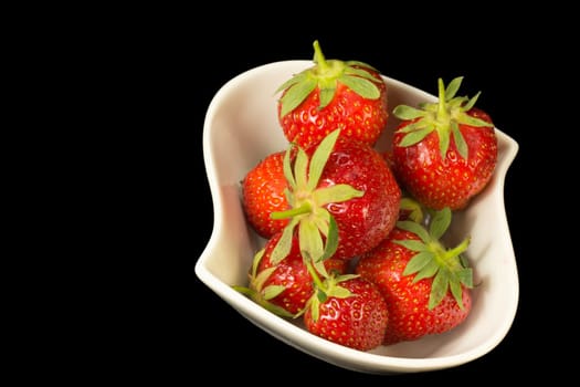 Fresh strawberries in white bowl on a black background. Horizontally.