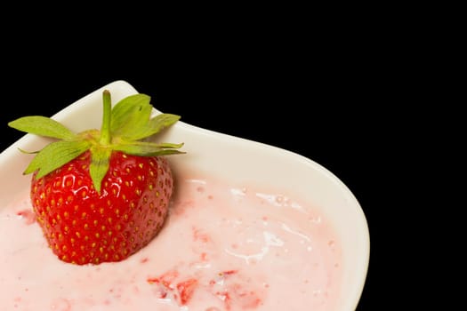 White bowl with strawberries in cream. In a bowl, is placed a fresh strawberry. Black background.