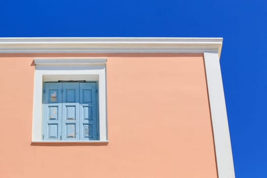 Colorful facade of a house with its blue closed shutters, red facade by beautiful weather, Santorini, Greece.