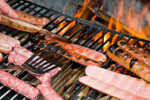 Brats  cooking on the grill with a flame in the background