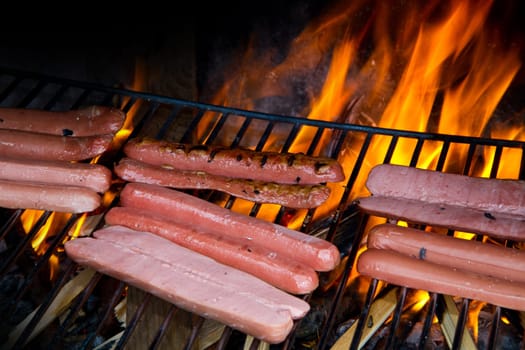 Brats  cooking on the grill with a flame in the background