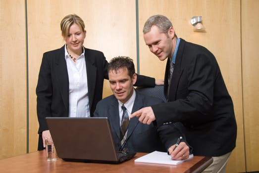 3 business people around a laptop in a meeting pointing