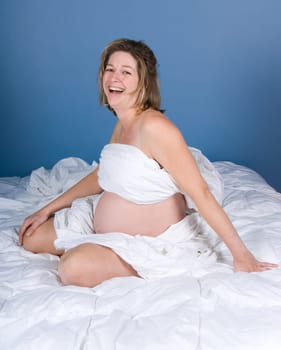 Happy pregnant woman on the bed with white sheets