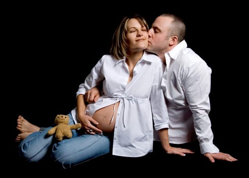 happy couple kissing with pregnant belly on black