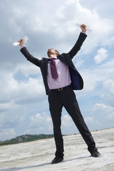 Photo of crying businessman standing and raising his arms with papers outdoors