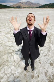 Photo of helpless businessman standing on dry ground and screaming with raised arms