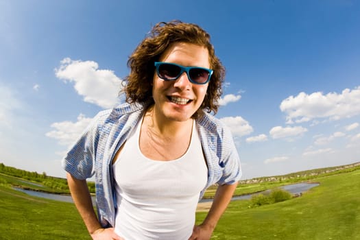 Portrait of young man in sunglasses looking at camera on background of countryside