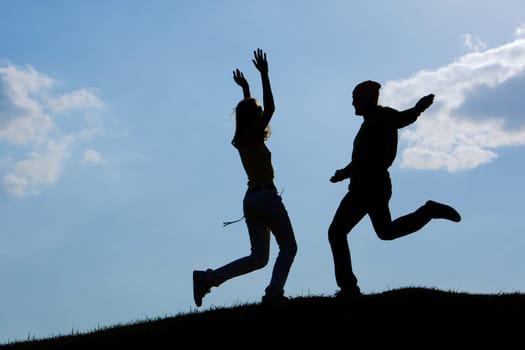 Image of cheerful girl and guy moving energetically against bright blue sky outdoors
